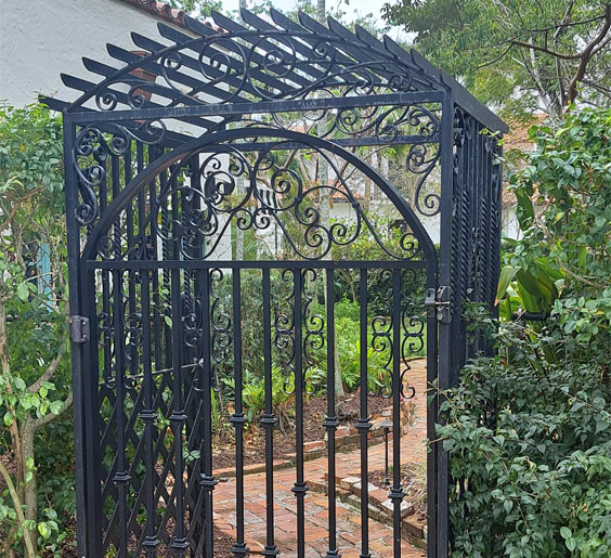 A black wrought aluminum fence Miami gate stands in front of a lush Miami garden.