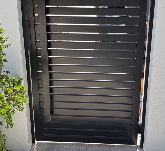 A black metal fabrication Pompano Beach gate is framed by a white fence.