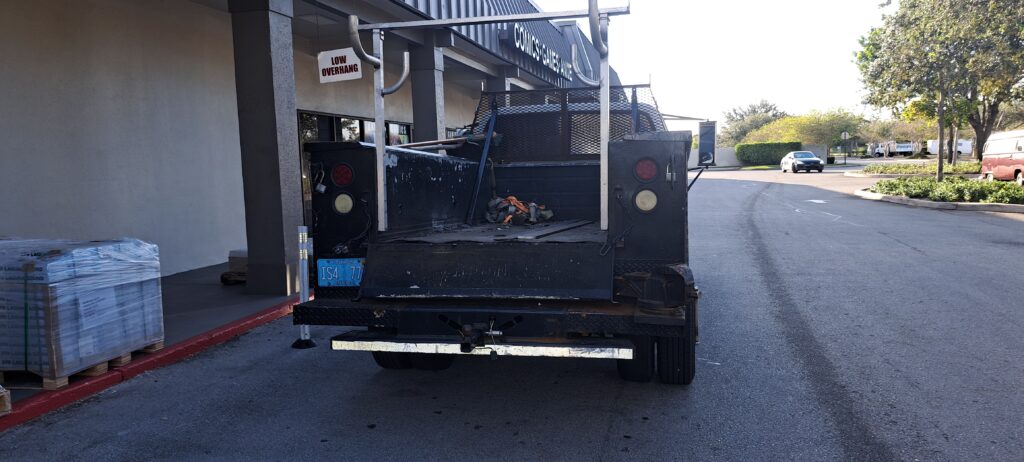 Utility work truck with tool bed and trailer carrying construction equipment in industrial setting
