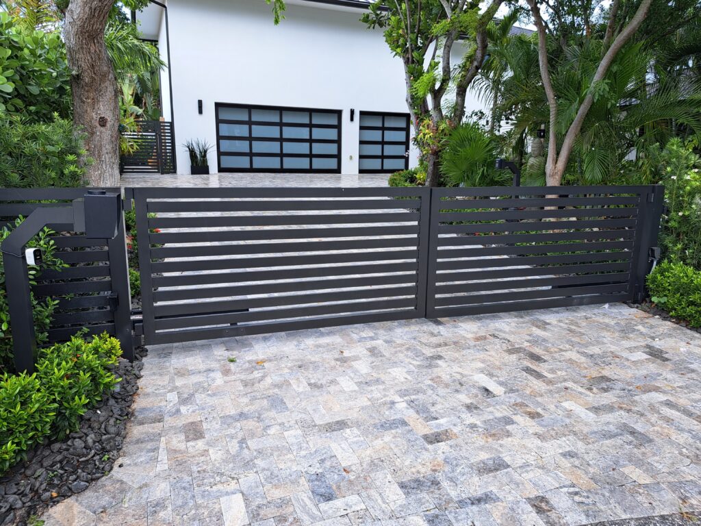 Finished black horizontal-slat aluminum driveway gate at a landscaped home.
